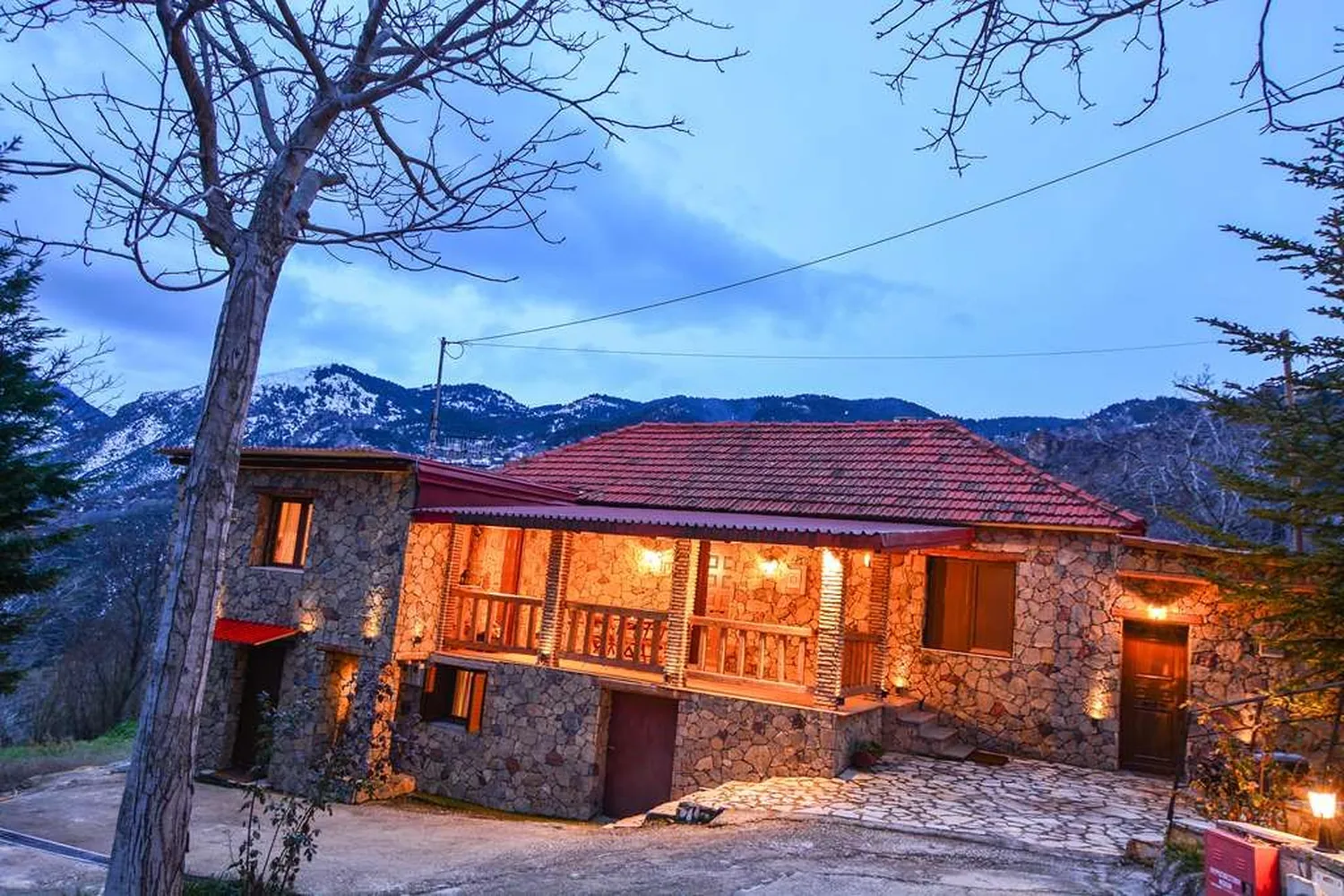 Ο ξενώνας με τη στέγη από κεραμίδια και τα φώτα αναμμένα, με τα βουνά πίσω